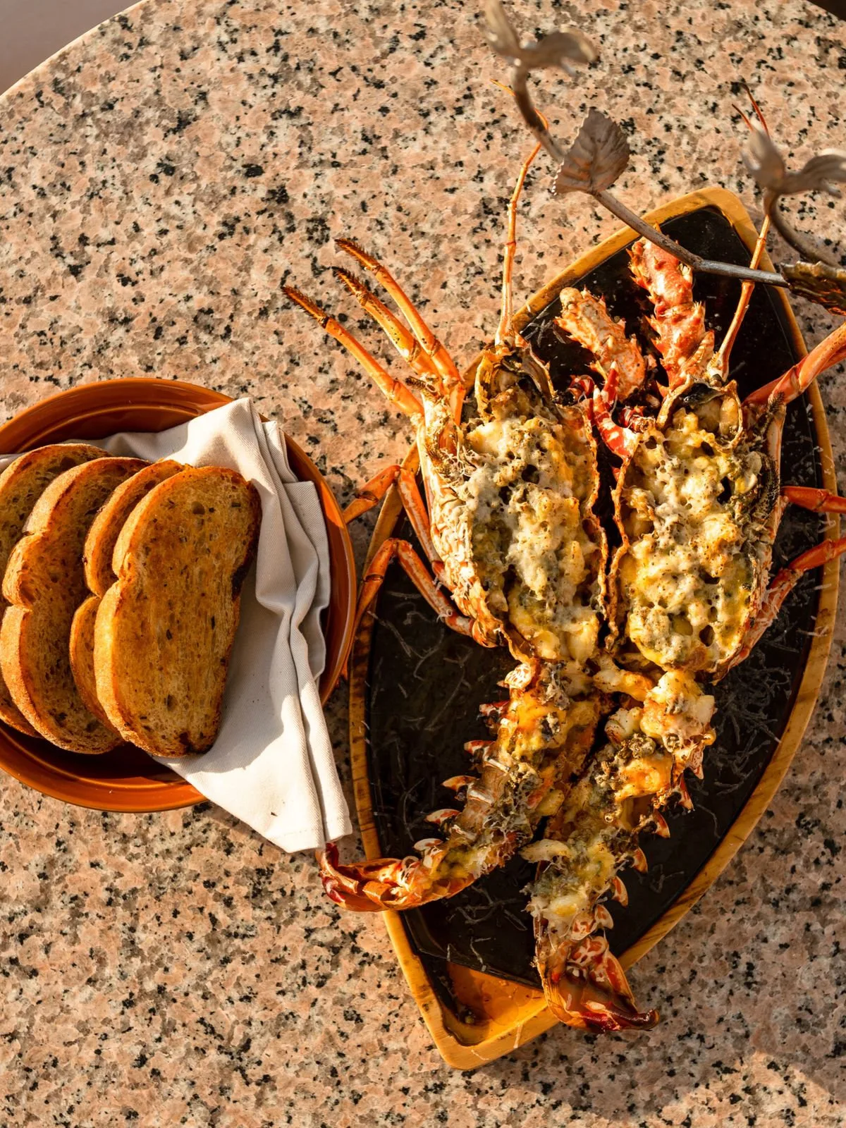 FUEGO Y MAR - Langosta entera a la robata, realzada con un intenso chimichurri asiático y una sedosa holandesa de hierbabuena. El queso Grana Padano y un exclusivo pan de masa madre con uchuvas y romero completan la experiencia.
